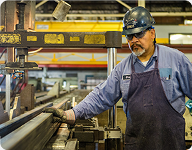 man in a blue shirt and hat working on a piece of metal
